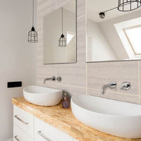 Modern bathroom interior with dual vessel sinks, wooden countertop, wall-mounted faucets, large mirror, and pendant cage lights.