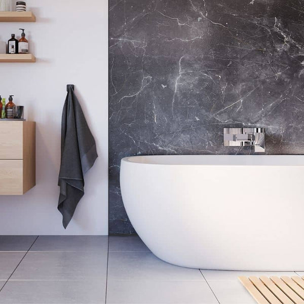 Modern bathroom interior with freestanding white bathtub, gray tiled floor, black marble wall, wooden vanity with shelving and toiletries, hanging gray towel, and minimalist faucet design