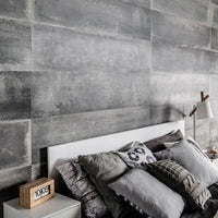 Modern bedroom with industrial grey concrete wall texture, cozy white bed with grey and patterned pillows, wooden digital clock, bedside lamp and table.