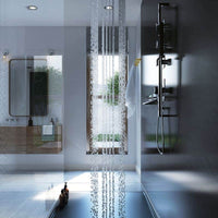 Modern bathroom interior with reflective floor tiles, cascading water from ceiling shower head, sleek glass partition, wall-mounted towel rack, minimalist mirror, and natural light from window.