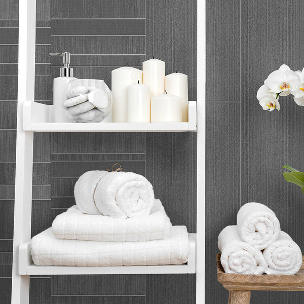 Modern bathroom decor with fluffy white towels, candles, orchids, and soap dispenser on shelves against dark gray textured wall tiles