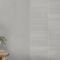 Modern gray tile wall with different textures, wooden stool, and green houseplant on light gray flooring