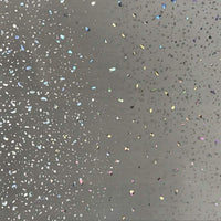 Close-up of a gray surface speckled with colorful glitter, featuring a variety of sparkly specks and holographic confetti scattered across a neutral background.