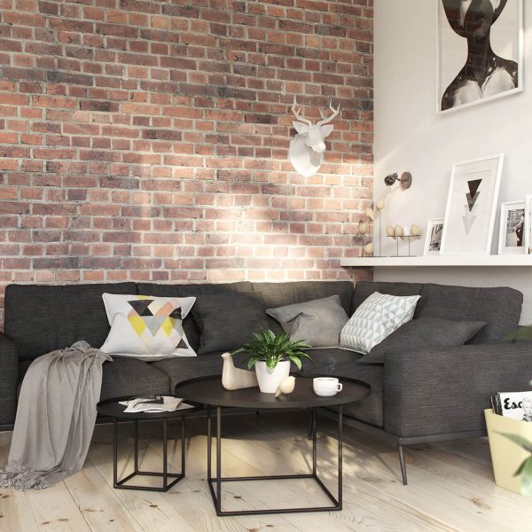Modern living room with exposed brick wall, dark gray sofa with decorative pillows, round coffee table, white deer head wall decor, wood flooring, and indoor plants.