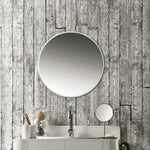 Round wall mirror above bathroom vanity against textured wood-patterned wallpaper, minimalist interior design, reflective surface, home decor details, sink faucet, and toiletries on countertop.