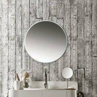 Round wall mirror above bathroom vanity against textured wood-patterned wallpaper, minimalist interior design, reflective surface, home decor details, sink faucet, and toiletries on countertop.
