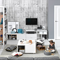 Modern living room interior with gray sofa, rustic wooden wallpaper, white entertainment unit, mounted flat-screen TV, decorative items, and a child playing with wooden blocks on a textured rug.