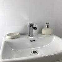 Modern bathroom sink with chrome faucet, white soap dispenser, and stone soap dish on a clean white countertop with minimalist design