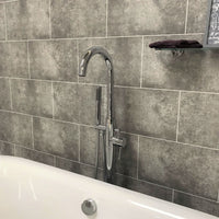 Modern bathroom with gray tile wall, chrome bathtub faucet and handheld shower head, white bathtub, and decorative towel on shelf