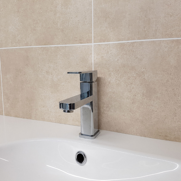 Modern chrome bathroom faucet on a white sink with beige tile wall background