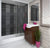 Modern bathroom interior with glass shower enclosure, wooden vanity cabinet, white basin, pink accessories, and indoor plant