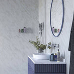 Modern bathroom interior with marble walls, oval mirror, vessel sink on navy blue vanity, wall-mounted faucet, eucalyptus branch decor, and toiletries.