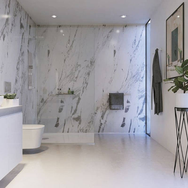 Modern bathroom interior with marble walls and floor, freestanding bathtub, glass shower enclosure, recessed ceiling lights, wall-mounted sink, towel rack, framed artwork, and indoor plants.