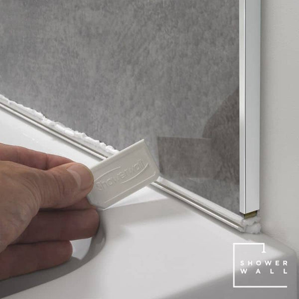 Hand applying silicone sealant to shower wall edge with caulk gun for waterproofing bathroom, clear sealant application for shower enclosure installation