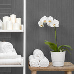 Modern bathroom interior with white orchid in pot, rolled towels, decorative candles on shelves, grey tile wall background.