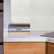 Modern kitchen interior with stainless steel paper towel holder, white countertop, wooden cabinets, and light green tiled wall