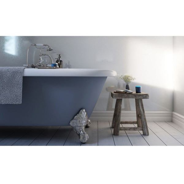 Modern bathroom with freestanding clawfoot bathtub, silver faucet, grey towel, wooden stool, white flowers in vase, and decorative blue candle on rustic wooden floor with soft natural light