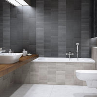 Modern bathroom interior with gray tiles, bathtub, sink, wall-mounted faucet, toilet, and wooden countertop.