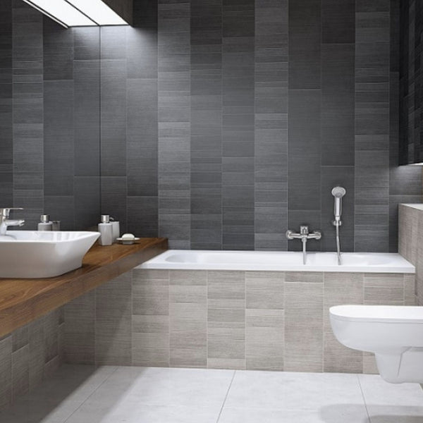Modern bathroom interior with gray tiles, bathtub, sink, wall-mounted faucet, toilet, and wooden countertop.