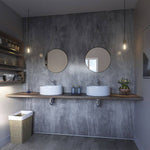 Modern bathroom interior with dual vessel sinks, wall-mounted faucets, round mirrors, industrial pendant lights, wooden shelf, concrete textured wall, and decorative plants.