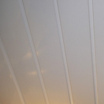 Abstract angled view of off-white vertical lines possibly representing curtains or architectural details with subtle warm light reflection in the background indicating sunrise or sunset.
