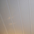 Abstract angled view of off-white vertical lines possibly representing curtains or architectural details with subtle warm light reflection in the background indicating sunrise or sunset.
